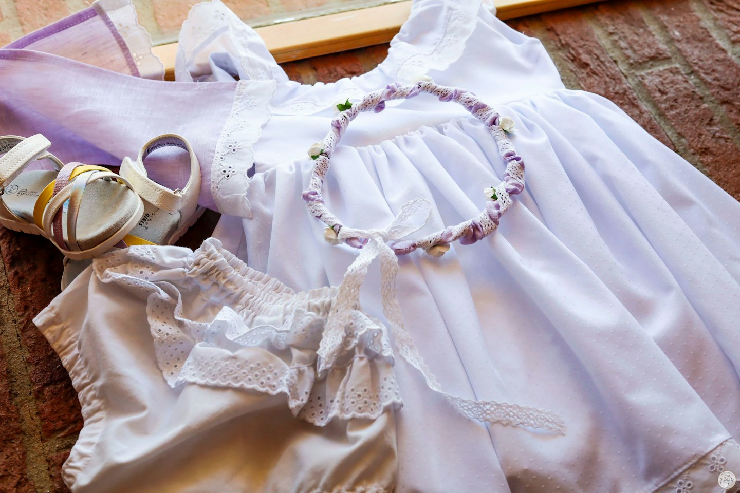 Vestiti e accessori per neonati disposti su una superficie di mattoni.