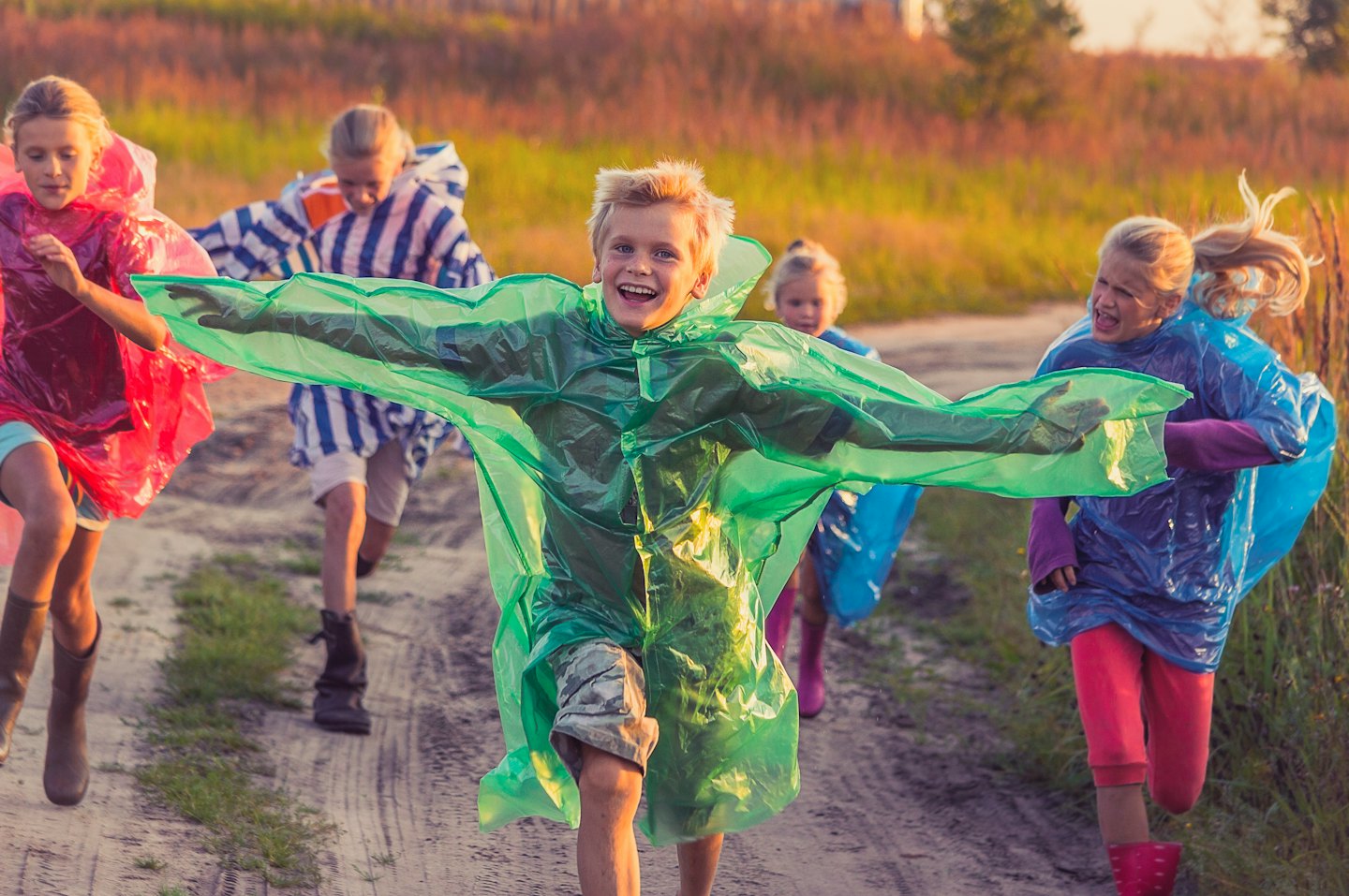 Bambini con poncho colorati corrono felici lungo un sentiero sterrato.